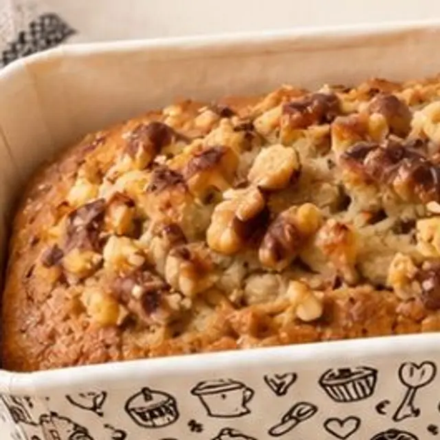 A banana walnut loaf cake in a printed baking tin