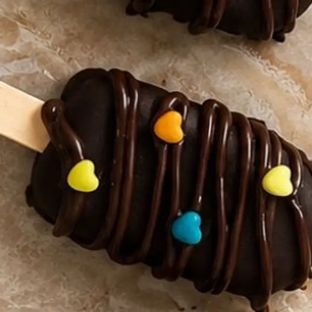 A chocolate-coated brownie popsicle with colourful gems on a wooden stick